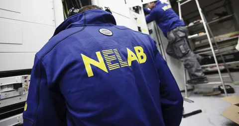 Två Nelab-medarbetare i blå arbetsjackor arbetar vid elskåp